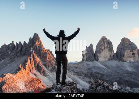 L'uomo conquista la collina e mostra le mani e piedi sulla pietra nella parte anteriore del Paternkofel e tre montagne di suono di avviso Foto Stock