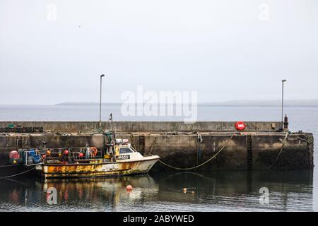 Rusty vecchia barca da pesca ormeggiate nel porto di John O'Semole, con l'isola Orcadian di stroma visibile attraverso il Pentland Firth Foto Stock