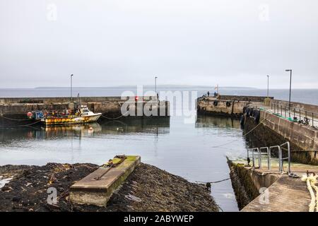 Rusty vecchia barca da pesca ormeggiate nel porto di John O'Semole, con l'isola Orcadian di stroma visibile attraverso il Pentland Firth Foto Stock