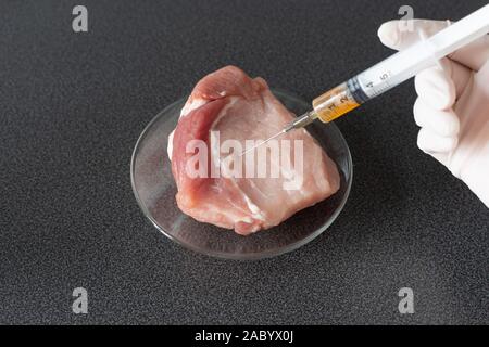 Ricercatore di iniettare OGM una fetta di carne di maiale. Organismo geneticamente modificato, nocivi per la salute peples. La carne con il concetto di antibiotici. Foto Stock