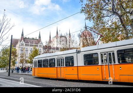 Budapest, Ungheria - Novembre 6, 2019: pubblici tram giallo a cavallo di fronte al parlamento ungherese edificio. Capitale ungherese dei trasporti pubblici. Mezzi di trasporto della città. Attrazione turistica. Foto Stock