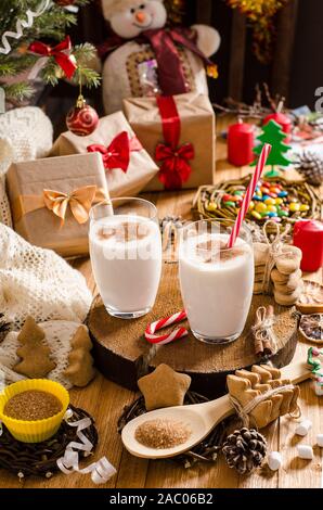 Natale e Anno Nuovo zabaione bevande in bicchieri di vetro su un supporto di legno sul tavolo con i regali di Natale i cookie, candele, dolciumi e albero di Natale bra Foto Stock