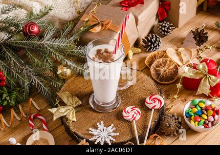 Natale e Anno Nuovo zabaione drink nel bicchiere di vetro su un supporto di legno sul tavolo con i regali di Natale i cookie, candele, dolciumi e albero di Natale di crusca Foto Stock