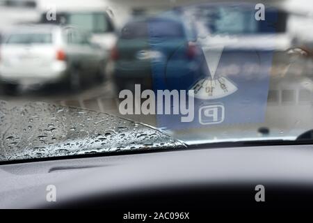 Le gocce di pioggia e di riflessione del disco di parcheggio su un parabrezza di automobile Foto Stock