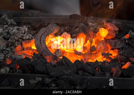 Riscaldamento a ferro di cavallo per la fucinatura. Embers glow in una fucina di ferro. Incendio, calore, carbone e cenere con scintille volanti. Foto Stock