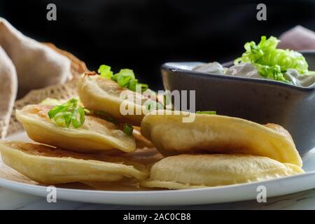 Deliziosa e autentica pierogies polacco con un trito di cipolla verde e panna acida Foto Stock