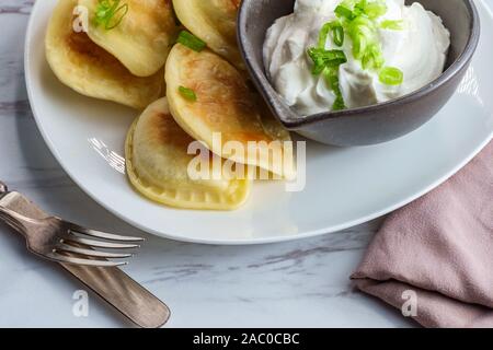 Deliziosa e autentica pierogies polacco con un trito di cipolla verde e panna acida Foto Stock