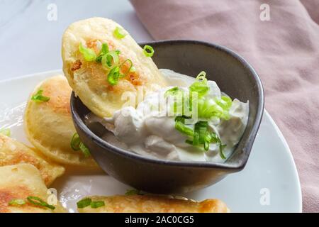 Deliziosa e autentica pierogies polacco con un trito di cipolla verde e panna acida Foto Stock