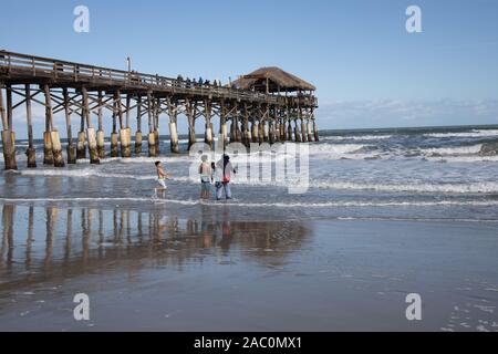 Gruppo di persone a giocare su Cocoa Beach Florida USA con il molo di legno in background e riflessioni sulla sabbia bagnata Foto Stock