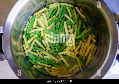 Fette di fagioli verdi di diversi colori sono bolliti in acqua in una grande pentola di metallo Foto Stock