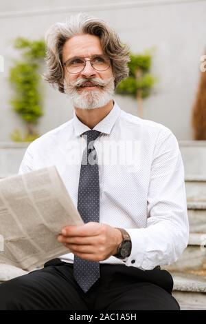 Foto di felice imprenditore anziani in occhiali azienda giornale mentre seduti all'aperto Foto Stock
