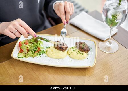 Pranzo in un ristorante, una donna mangia deliziosa succosa carne cotolette, purè di patate cosparso di verdi e sane fresca insalata di pomodori e Foto Stock