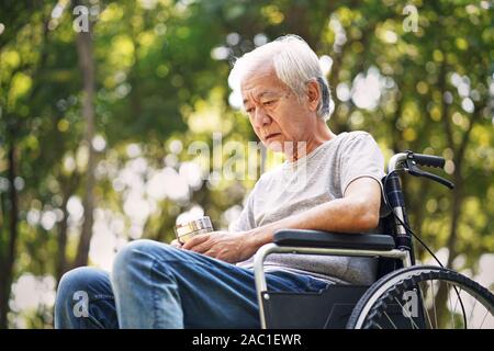 Asian vecchio seduto in una sedia a rotelle con la testa verso il basso guardando triste e depresso Foto Stock