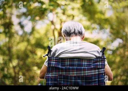 Vista posteriore di un anziano uomo seduto nella sedia a rotelle con la testa in giù Foto Stock