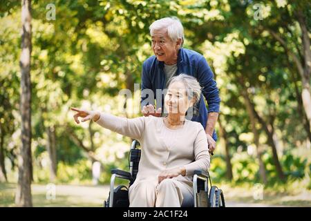 Senior asian uomo a camminare nel parco con sedia a rotelle moglie legato Foto Stock