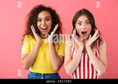 Immagine della multinazionale eccitato ragazze chiedendo e alzando le mani nella sorpresa isolate su sfondo rosa Foto Stock