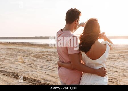 Vista posteriore di una bella coppia giovane indossa abbigliamento estivo presso la spiaggia, a puntare il dito lontano Foto Stock