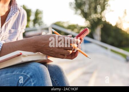 In prossimità di una giovane donna africana studiando seduti sui gradini esterni, utilizzando il telefono cellulare Foto Stock