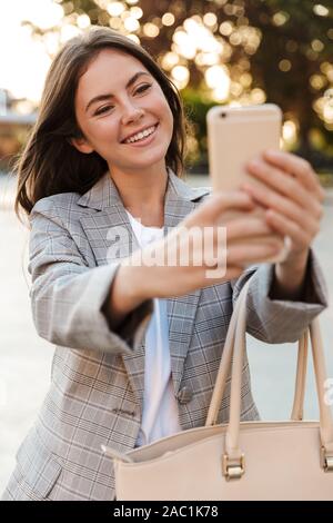 Foto di un allegro lieta positivo young lady camminando per strada prendere selfie dal telefono cellulare. Foto Stock