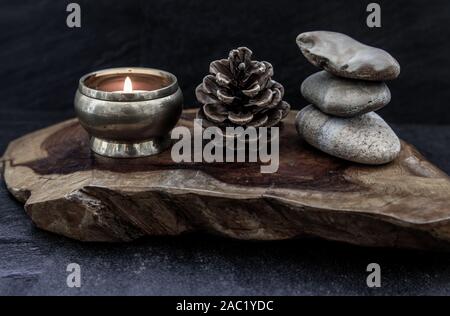 Piramide di pietre zen, pigne e candela che brucia sul vecchio sfondo di legno, il concetto di meditazione, di tono scuro stile. Sfondo Zen Foto Stock