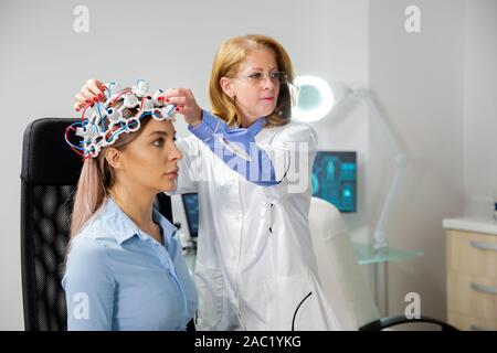 Medico di neurologia regolazione casco durante un cervello procedura di scansione. Paziente donna Foto Stock