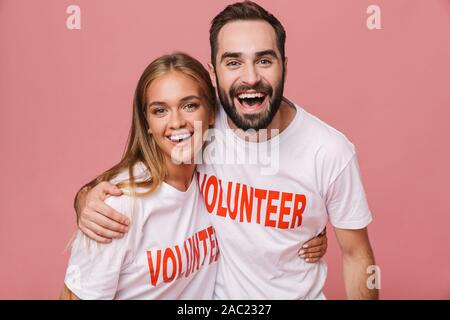 Immagine di gioiosa l uomo e la donna volontari uniforme che indossano la t-shirt sorridente isolate su sfondo rosa Foto Stock