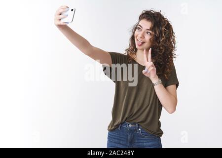 Divertente giocoso carino giovane georgiano curly-ragazza dai capelli tenendo selfie inviare fidanzato via internet app estende il braccio verso l'alto tenendo lo smartphone visualizza Foto Stock