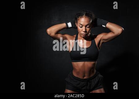 Immagine di forte americano africano donna che indossa abbigliamento sportivo in piedi in mano di inscatolamento avvolge isolate su sfondo nero Foto Stock