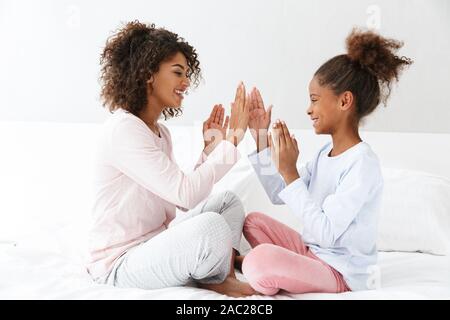 Immagine di gioiosa americano africano la donna e la sua piccola figlia sorridente e battendo le mani sul divano di casa Foto Stock