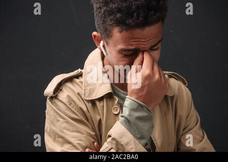 Immagine della infelice african american guy nel rivestire utilizzando earpods e pianto isolate su sfondo nero Foto Stock