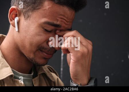 Immagine della infelice african american guy nel rivestire utilizzando earpods e pianto isolate su sfondo nero Foto Stock