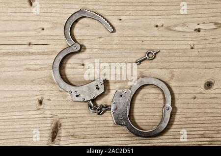 Vista dall'alto di aprire manette e chiave su un tavolo di legno di close-up. Il crimine e la violenza concetto Foto Stock