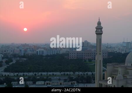 Il sole che tramonta sulla Manama City con il minareto di Al Fateh grande moschea in primo piano Foto Stock