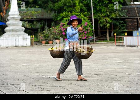 Donna anziana che trasportano un polo di spalla con due cestelli sospesi di ritorno dal mercato, Luang Prabang, Laos Foto Stock