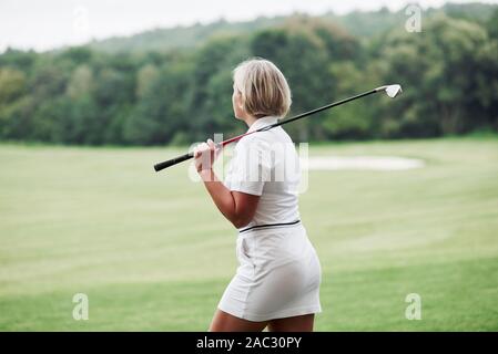 Adulto donna bionda hanno a piedi sul campo tenendo il bastone da golf Foto Stock