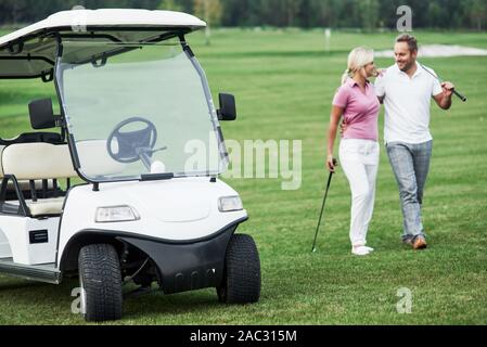 Il carrello da golf con coppia adorabile passeggiando vicino al veicolo e sorridente Foto Stock