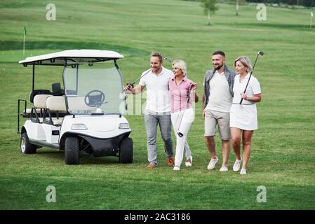 Il gruppo di amici di famiglia a camminare sul campo dopo la partita di golf con il veicolo dietro Foto Stock