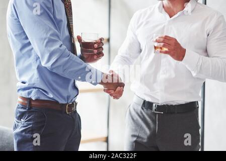 In prossimità dei due international business mans hanno un buon affare e tenuta bicchieri di whiskey Foto Stock