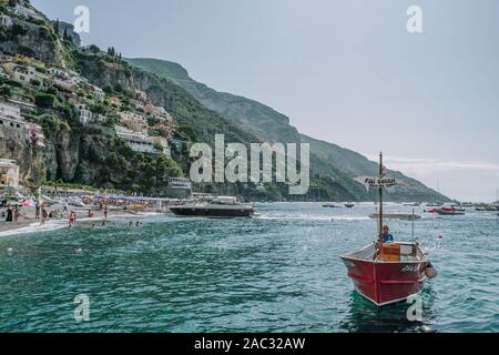 Positano, Italia - 14 agosto 2019: l'uomo in barca rossa nella parte anteriore della spiaggia di Positano, Costiera Amalfitana Foto Stock