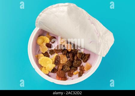 Yogurt rosa in un vaso con cereali e uva passa su un sfondo turchese. Yogurt alla frutta in un contenitore aperto su uno sfondo blu. Vista dall'alto. Foto Stock