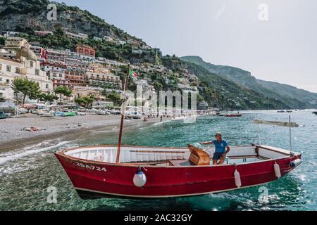 Positano, Italia - 14 agosto 2019: l'uomo in barca rossa nella parte anteriore della spiaggia di Positano, Costiera Amalfitana Foto Stock