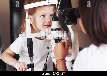 Guarda dritto. Bambina sono la prova per i suoi occhi con una speciale apparecchiatura ottica dal medico donna Foto Stock