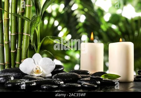 Grean foglie di bambù, white orchid flower, asciugamano e candele su nero pietre zen sulle foglie tropicali sfondo Foto Stock