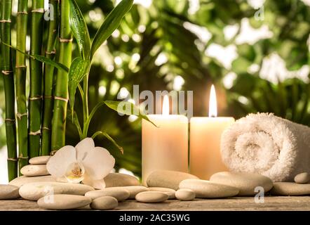 Grean foglie di bambù, white orchid flower, asciugamano e candele su nero pietre zen sulle foglie tropicali sfondo Foto Stock