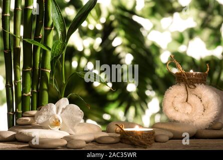 Grean foglie di bambù, white orchid flower, asciugamano e candele su nero pietre zen sulle foglie tropicali sfondo Foto Stock