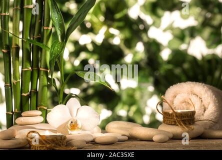 Grean foglie di bambù, white orchid flower, asciugamano e candele su nero pietre zen sulle foglie tropicali sfondo Foto Stock