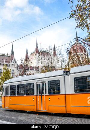 Budapest, Ungheria - Novembre 6, 2019: pubblici tram giallo a cavallo di fronte al parlamento ungherese edificio. Capitale ungherese dei trasporti pubblici. Mezzi di trasporto della città. Orientale destinazioni europee. Foto Stock