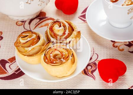 Ruddy sfornati su una piastra bianca con una coppa di frutta mela tè e una teiera e cuori rossi sul tavolo. Concetto di festa del santo Foto Stock