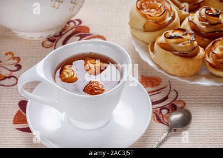Apple a base di erbe tè in una tazza bianca con piattino e rubicondo i panini su una piastra. Foto Stock