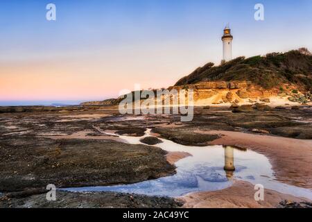 Fondali marini a bassa marea lasciando sale pozza d'acqua a riflettere faro bianco e rosa sky all alba Australian Pacific Coast - Norah capezzagna, il CEN Foto Stock